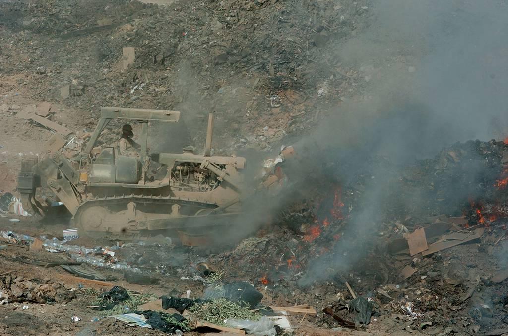 A soldier uses a bulldozer to maneuver refuse into a burn pit at Balad, Iraq, in 2004. (Defense Department photo)