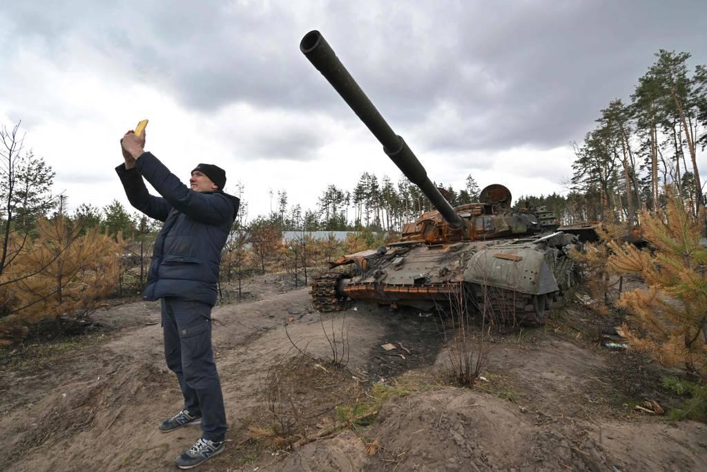 A man takes a selfie as he stands in front of a destroyed Russian tank in the village of Andriivka, in the Kyiv region, on April 17, 2022. (Sergei Supinski/AFP via Getty Images)